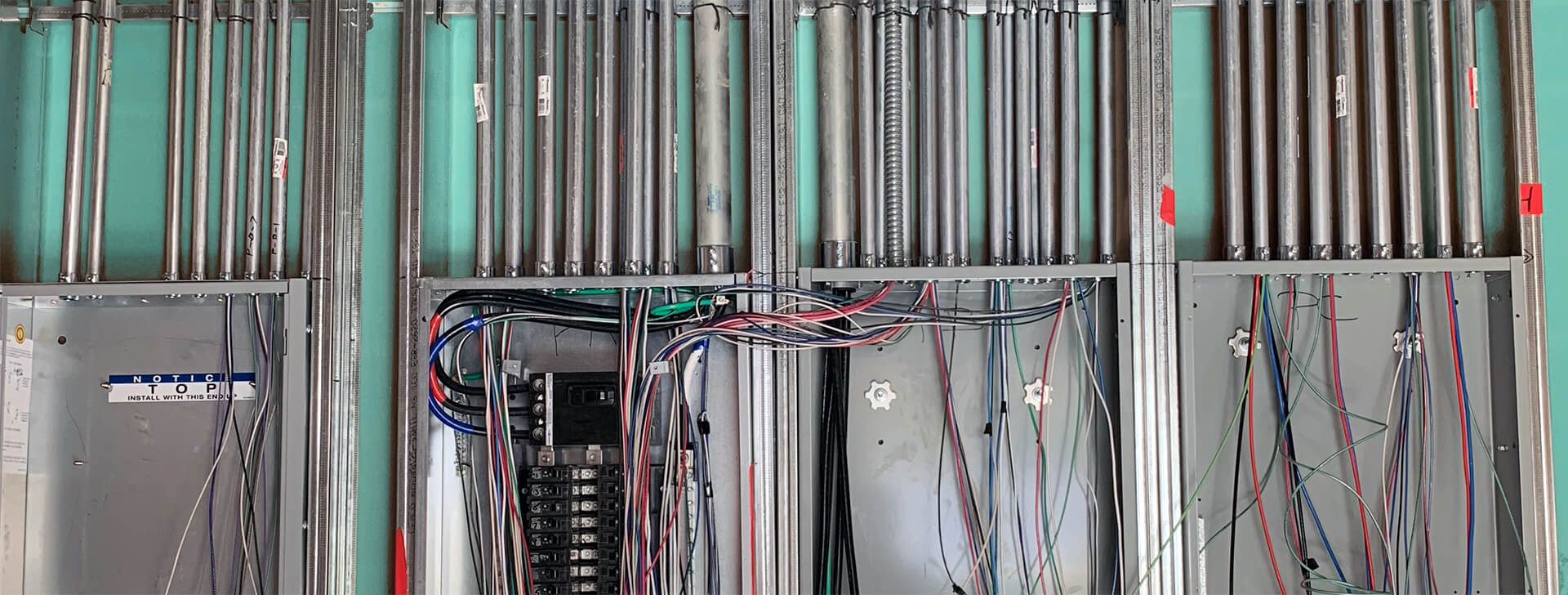 Wall of partially installed control boxes with tangles of colorful electrical wires sticking out.