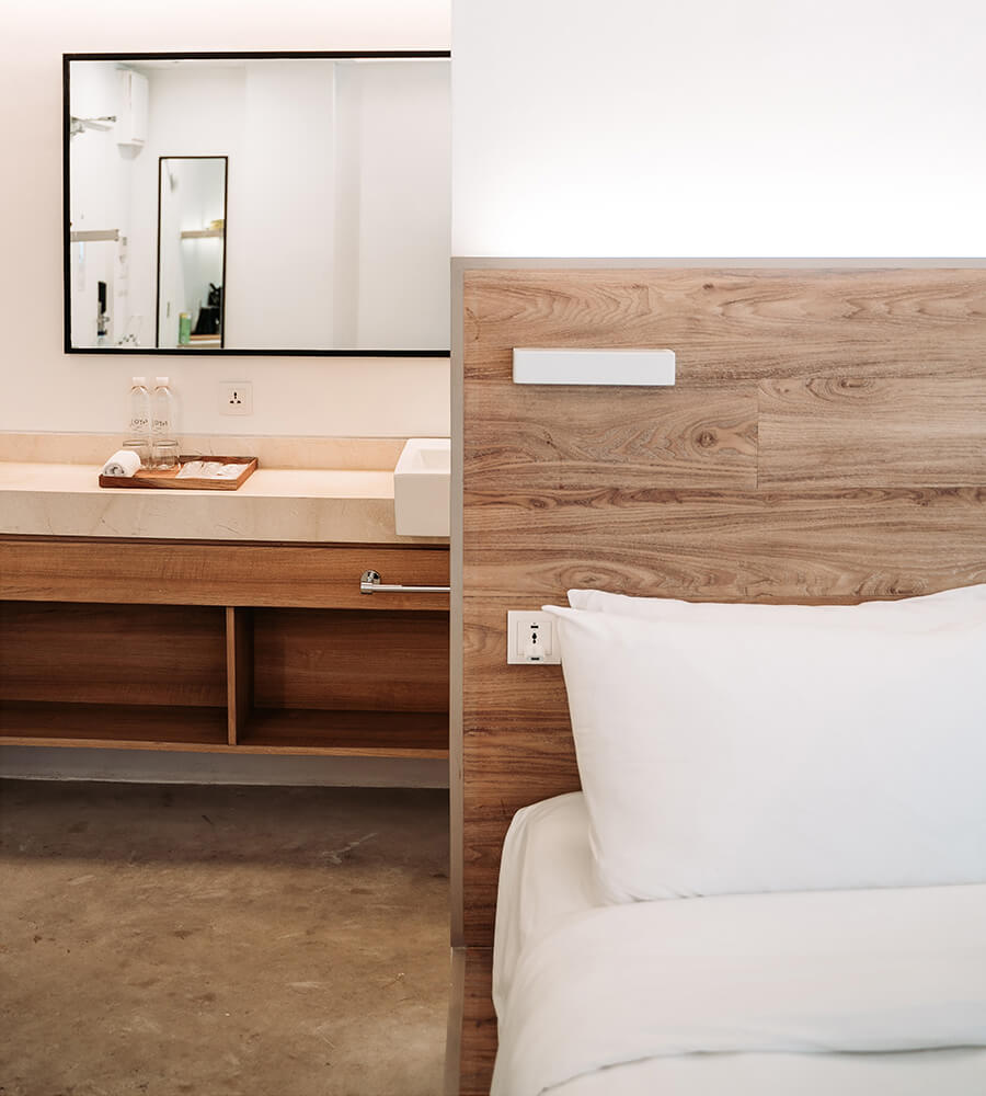 Hotel bed smart-enabled headboard in foreground and bathroom vanity in background.
